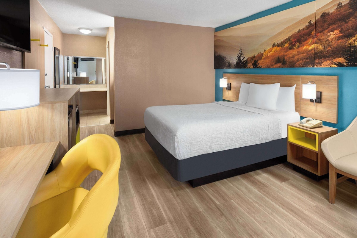 Habitación de hotel con cama, escritorio, silla, mesita de noche y televisor montado en la pared.