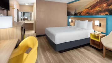 A hotel room with a bed, a desk, a chair, a nightstand, and a wall-mounted TV.