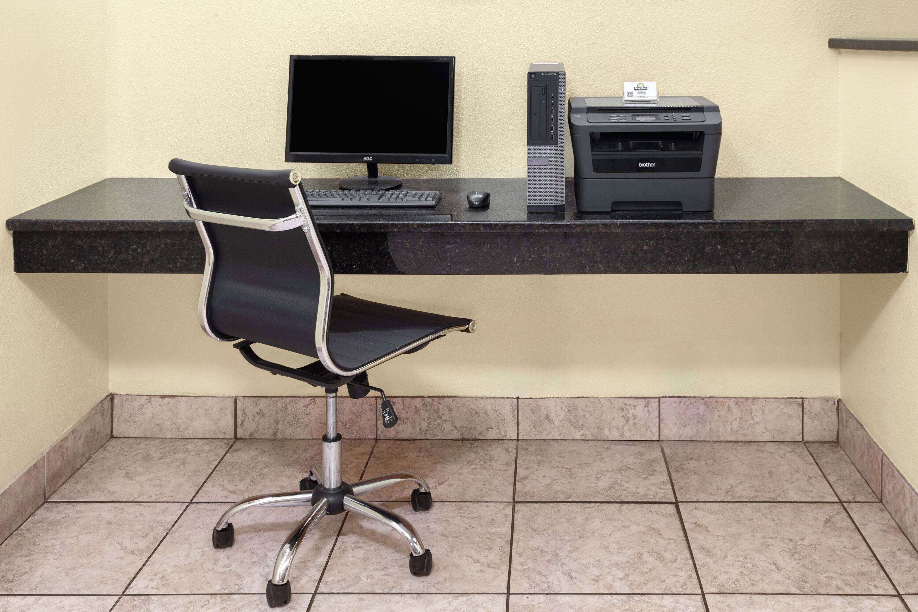 Un espace de travail comprenant un fauteuil de bureau noir, un écran d’ordinateur, un clavier, une souris et une imprimante Brother, le tout posé sur un plan de travail foncé.