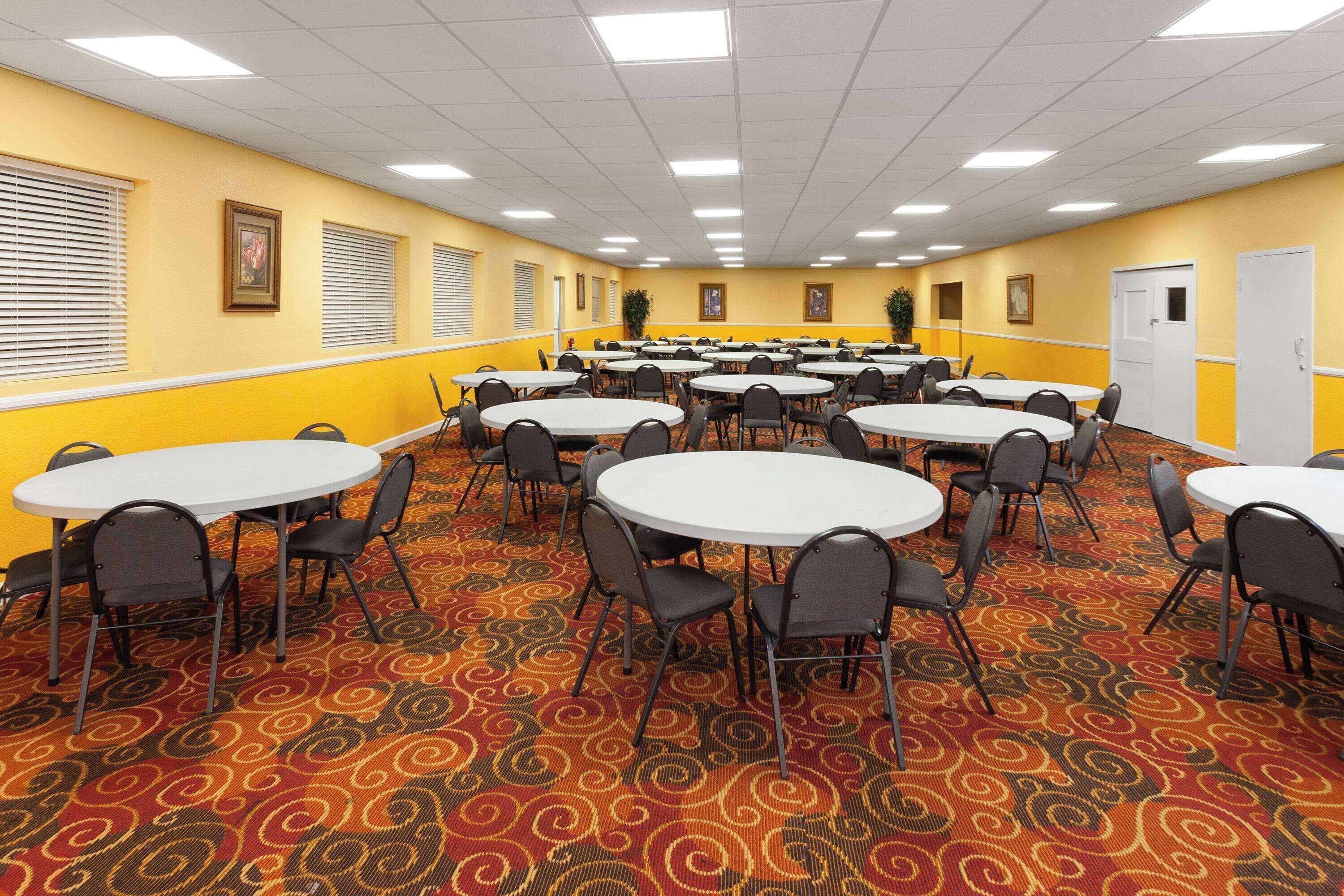 Uma sala de conferências com várias mesas redondas e cadeiras, paredes amarelas e carpete estampado.