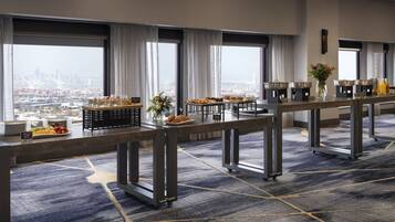 A breakfast buffet setup with various food items and a city view through large windows.
