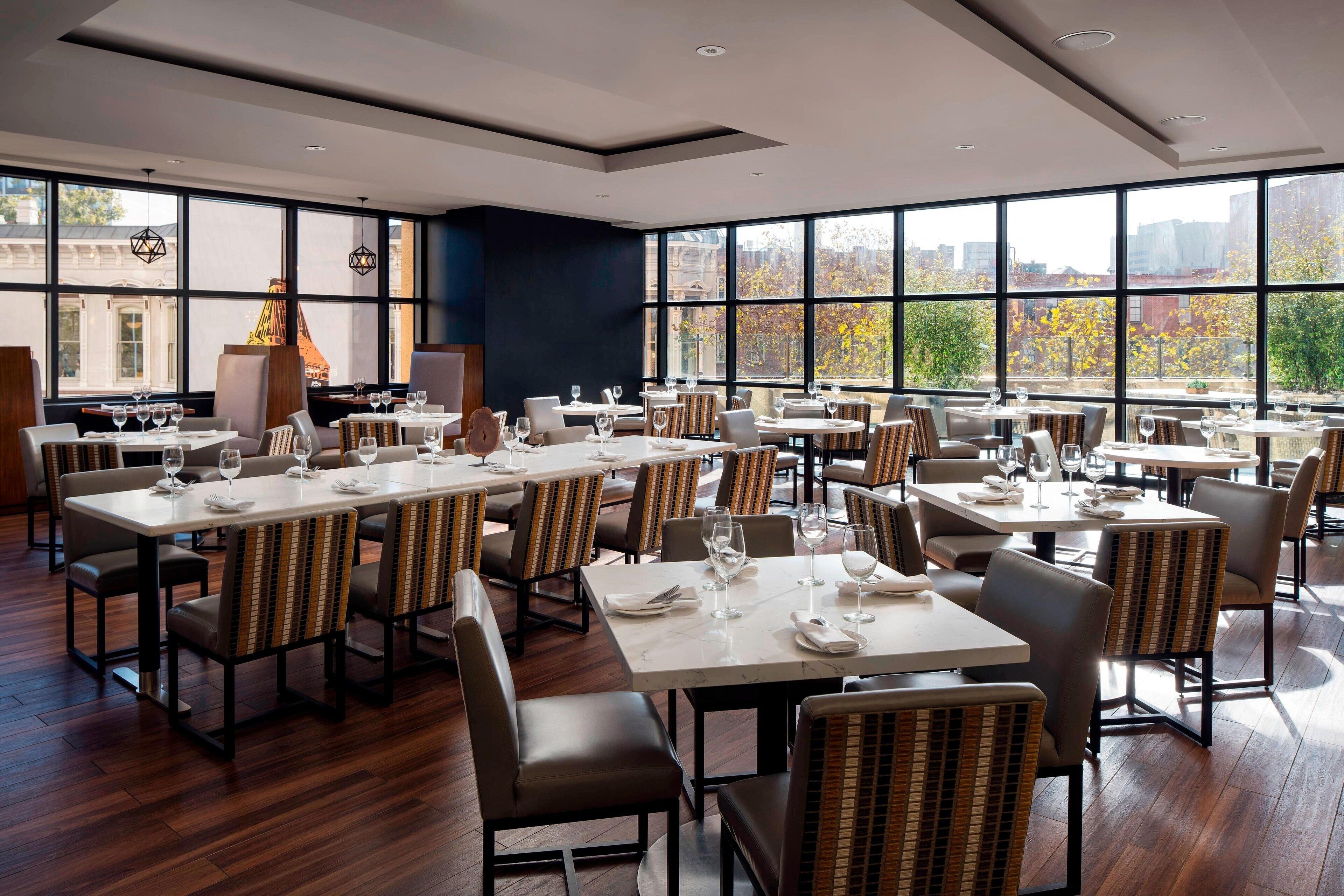 Um restaurante moderno com várias mesas e cadeiras, grandes janelas com vista para a cidade e um palco central com um orador.