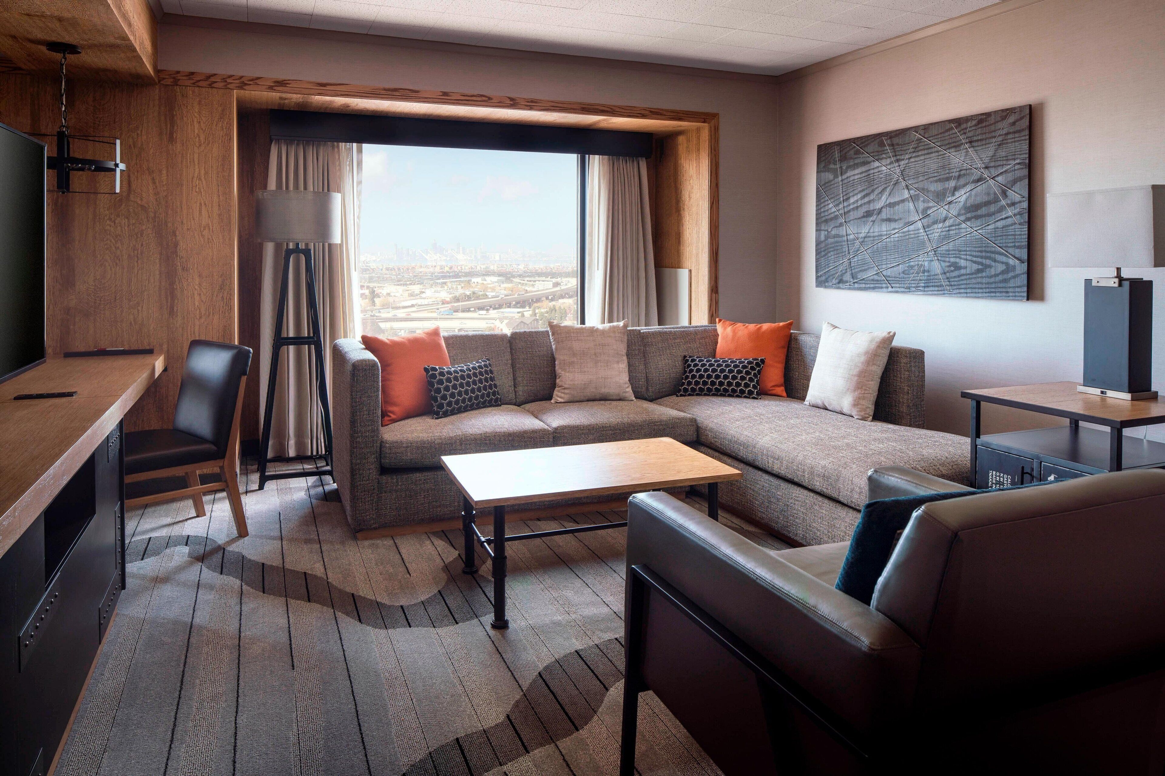 Una moderna camera d'hotel con un divano componibile, una scrivania e un'ampia finestra con vista sulla città.
