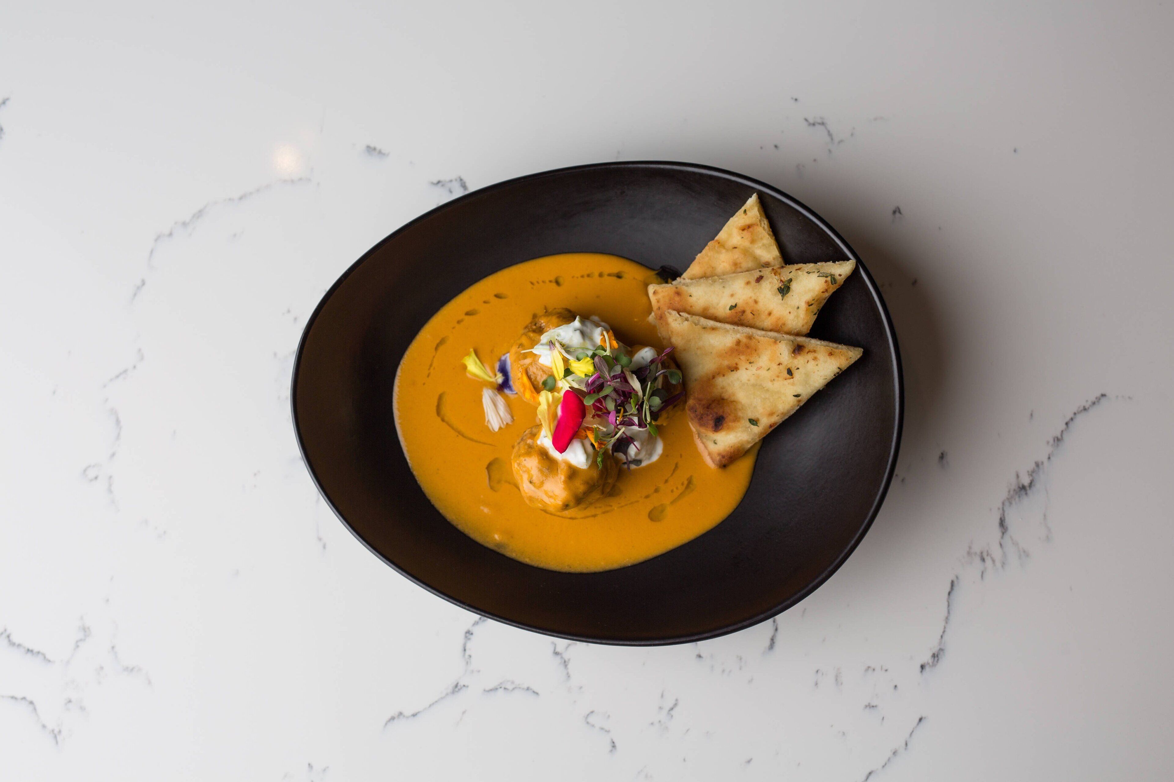 A dish with a creamy sauce, garnished with herbs and a dollop of cream, served on a dark plate.