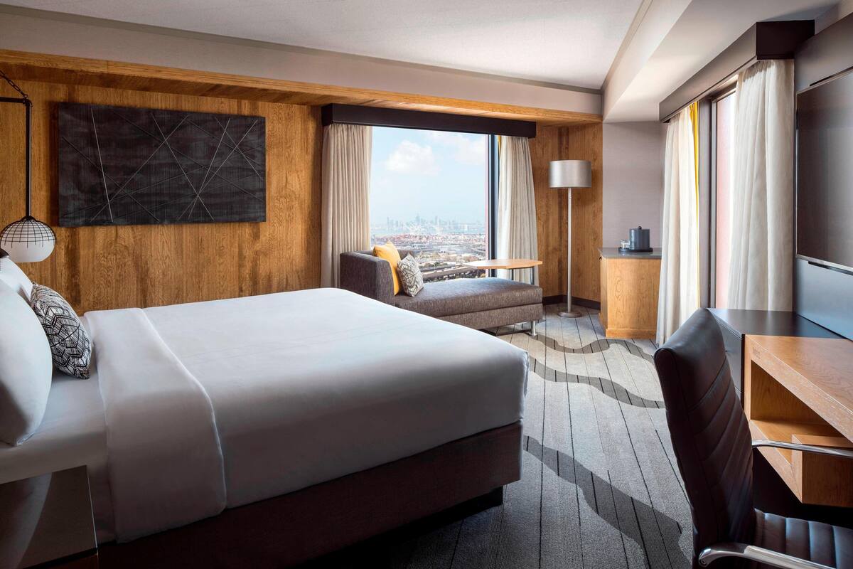 A hotel room with a large bed, a sofa, a desk, and a view of the city.