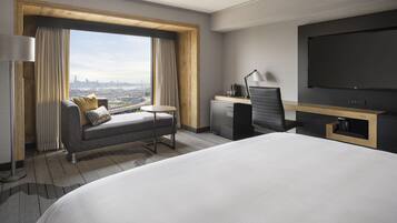 A modern hotel room with a large bed, a sofa, a desk, and a TV.