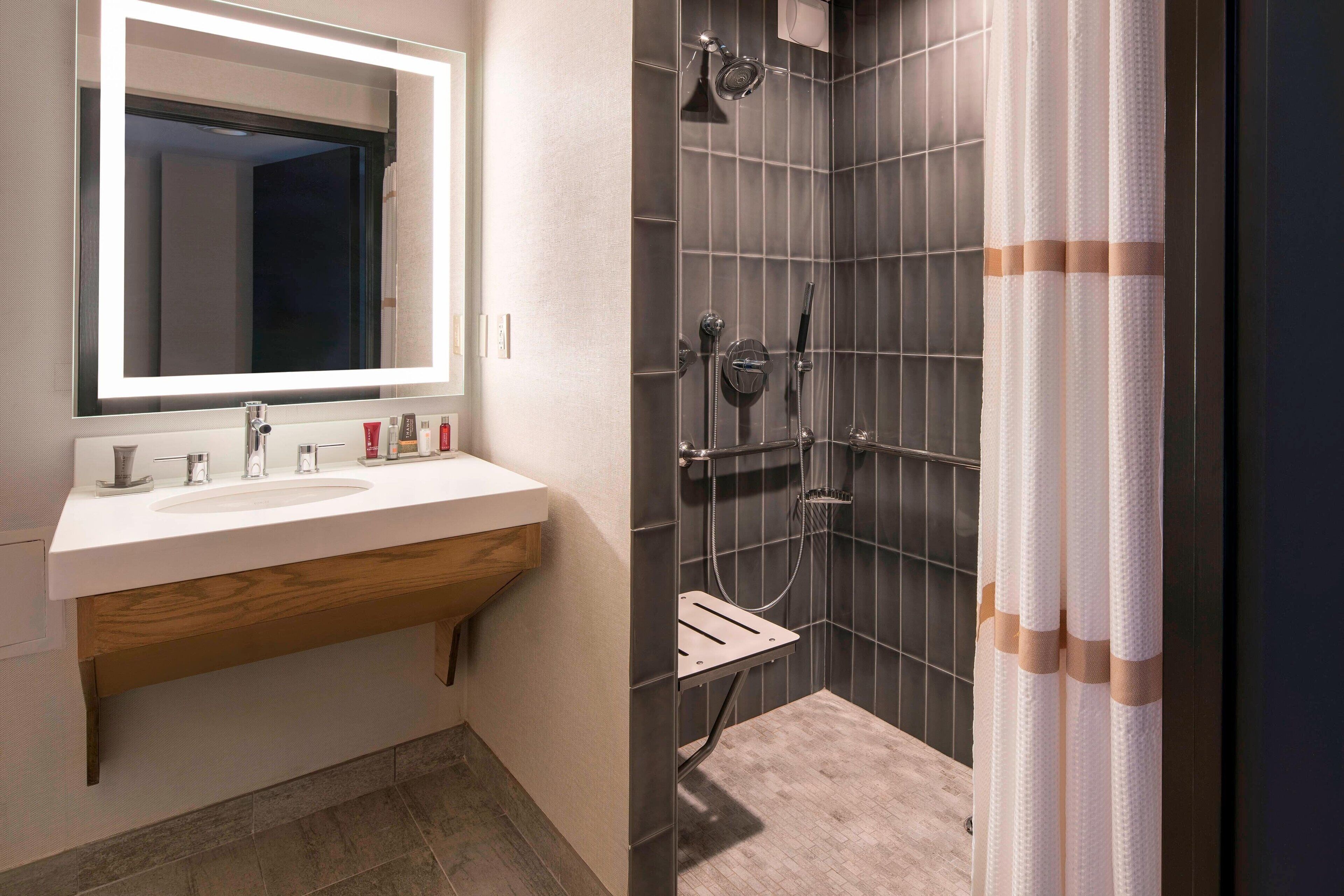 A modern bathroom with a large mirror, a sink, and a shower with a towel rack.