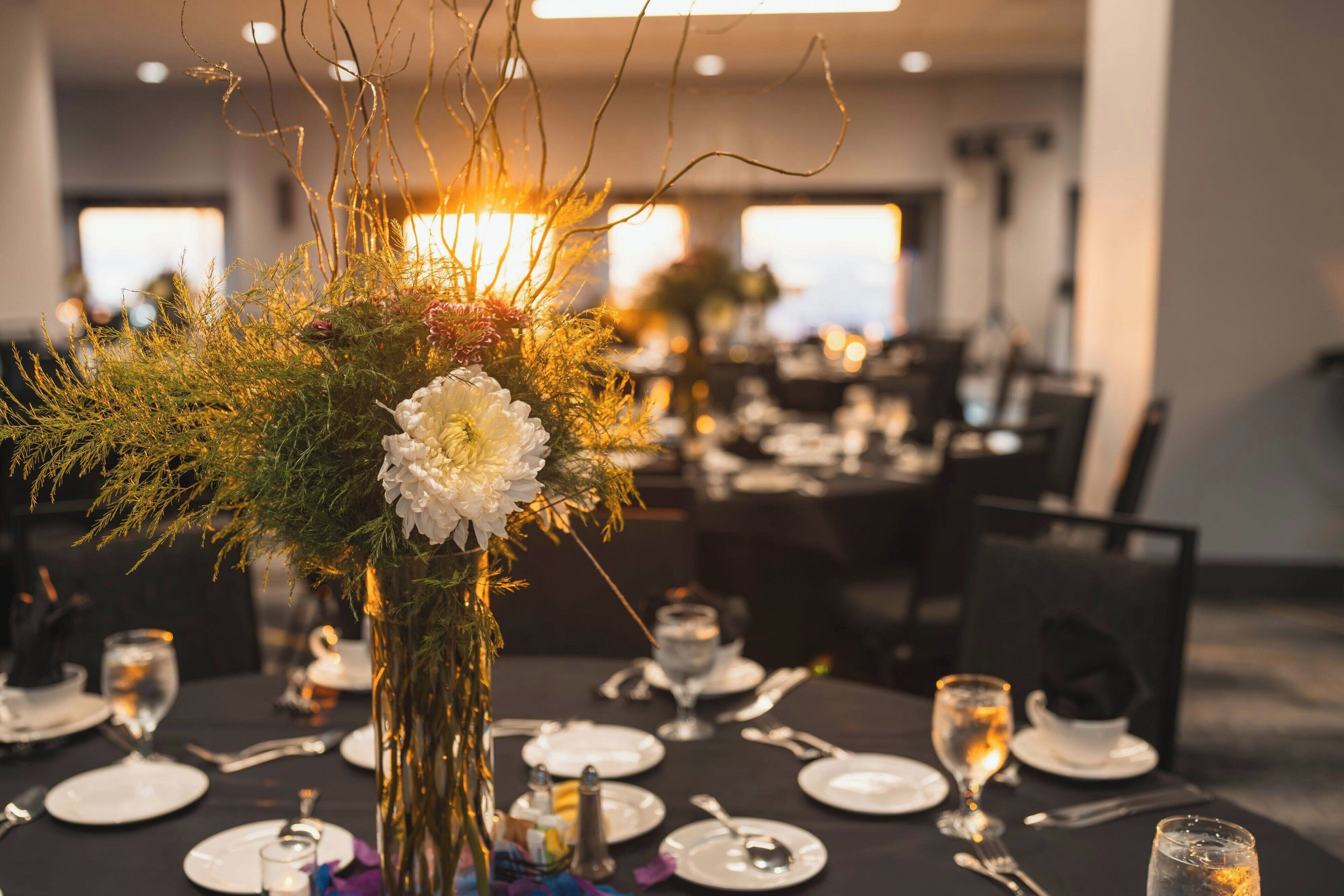 A dining table set with plates, cutlery, and a centerpiece of greenery and white flowers.