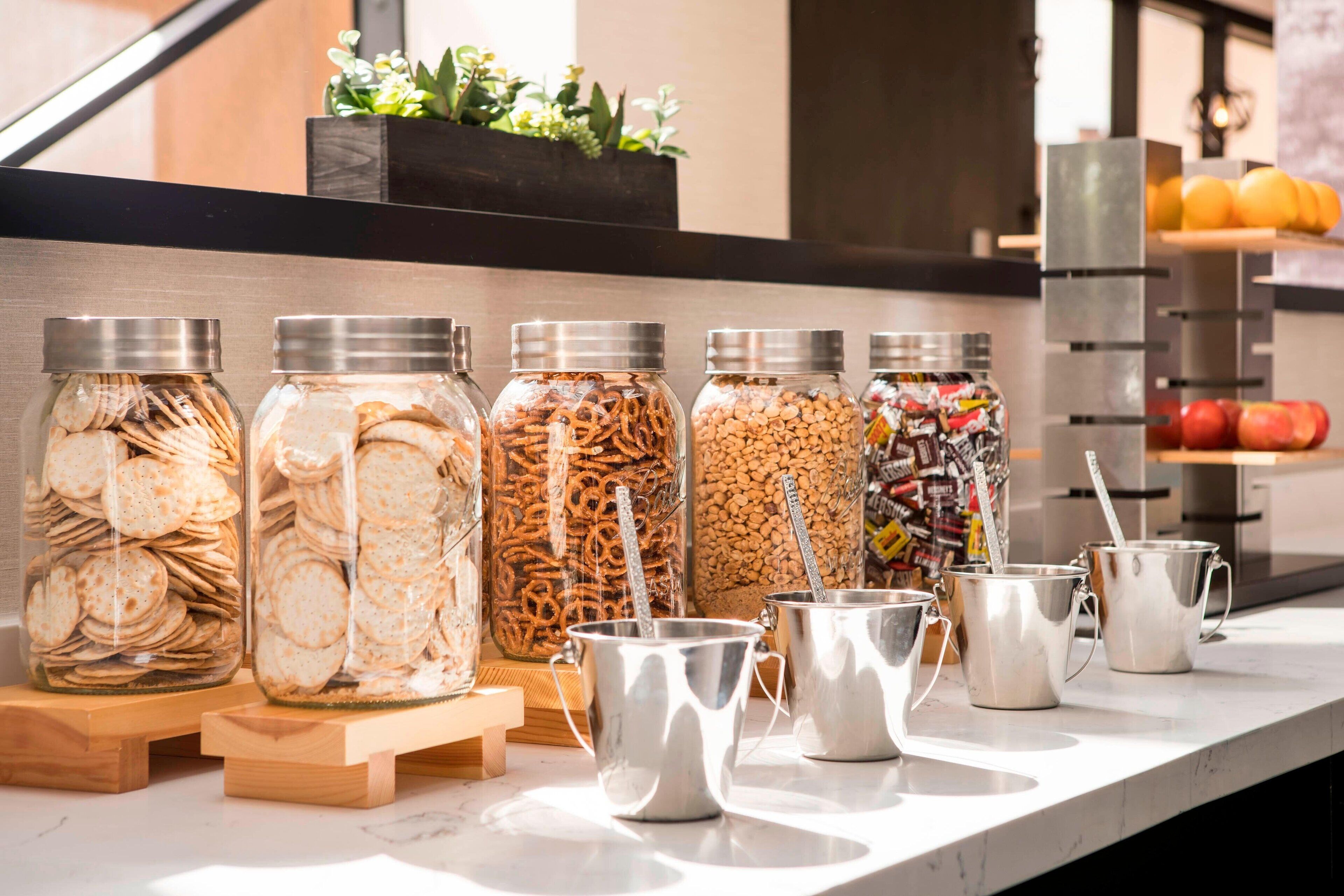 A buffet table with various food items in jars and metal cups.