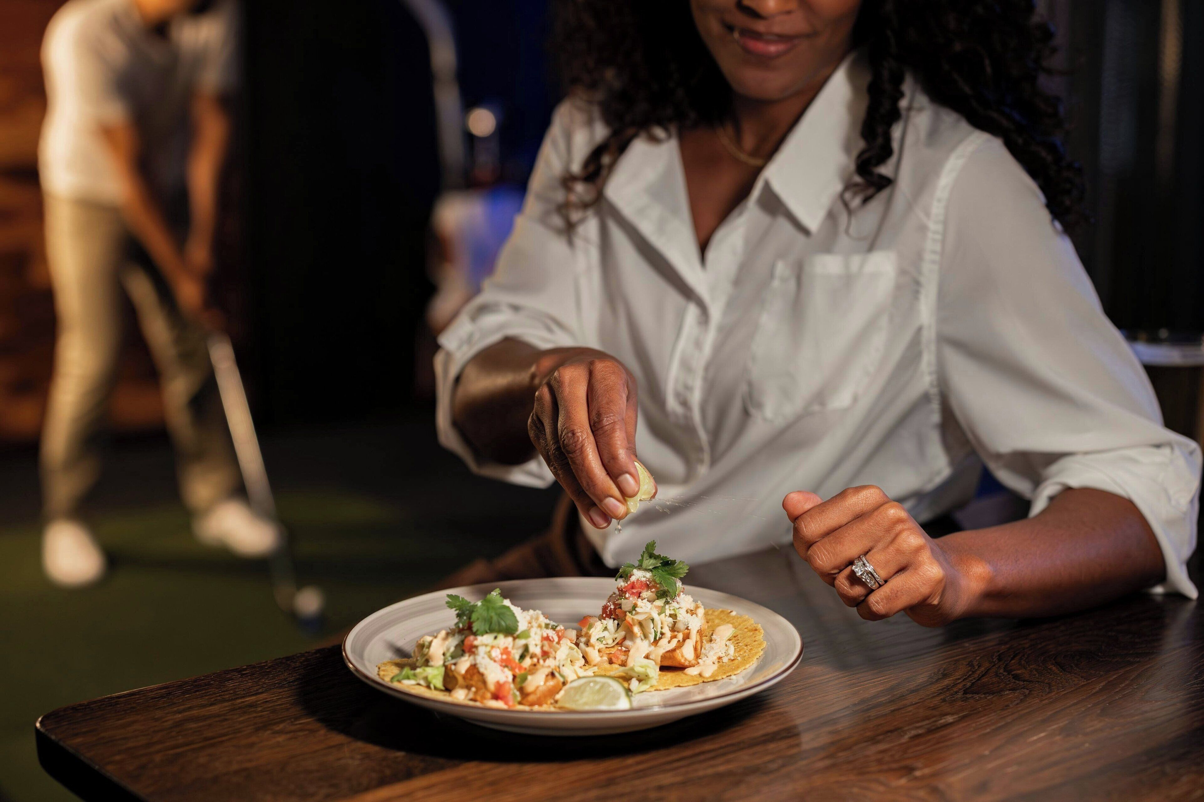 A person sitting at a table with a plate of food, a golf club in the background, and a wooden table.
