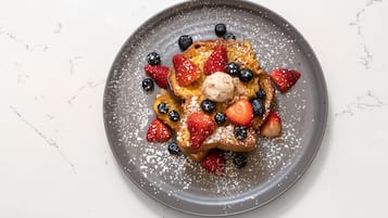 A plate of French toast with strawberries, blueberries, and a scoop of ice cream, dusted with powdered sugar.