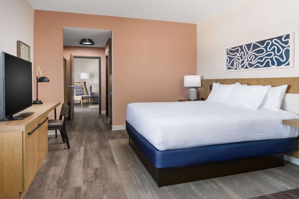 Une chambre d’hôtel avec un grand lit, un bureau avec une télévision et une chaise.