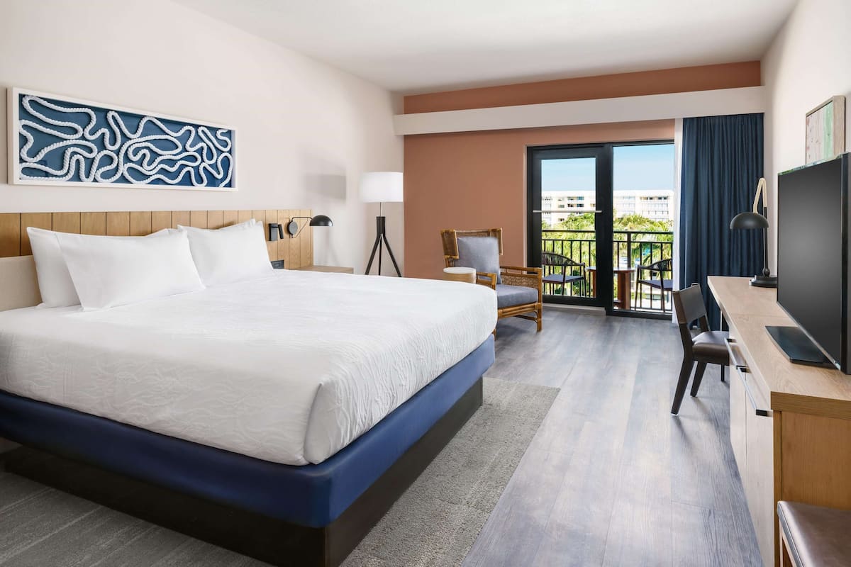 Une chambre d’hôtel avec un grand lit, un bureau, une chaise, une télévision et un balcon avec vue.
