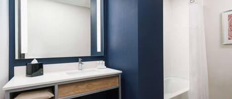A modern bathroom with a white sink, dark blue walls, a large mirror, and a white bathtub.