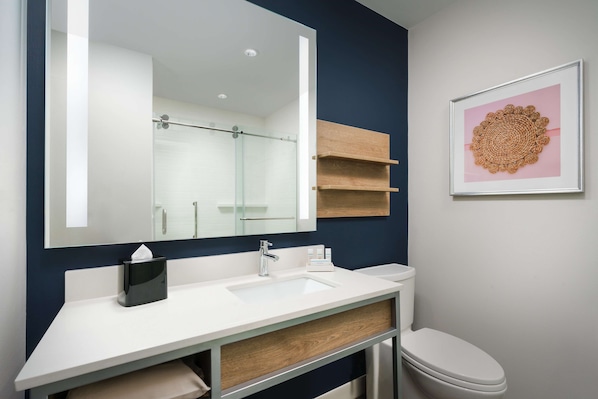 Une salle de bain moderne avec un grand miroir, un lavabo blanc et une œuvre d’art encadrée accrochée au mur.
