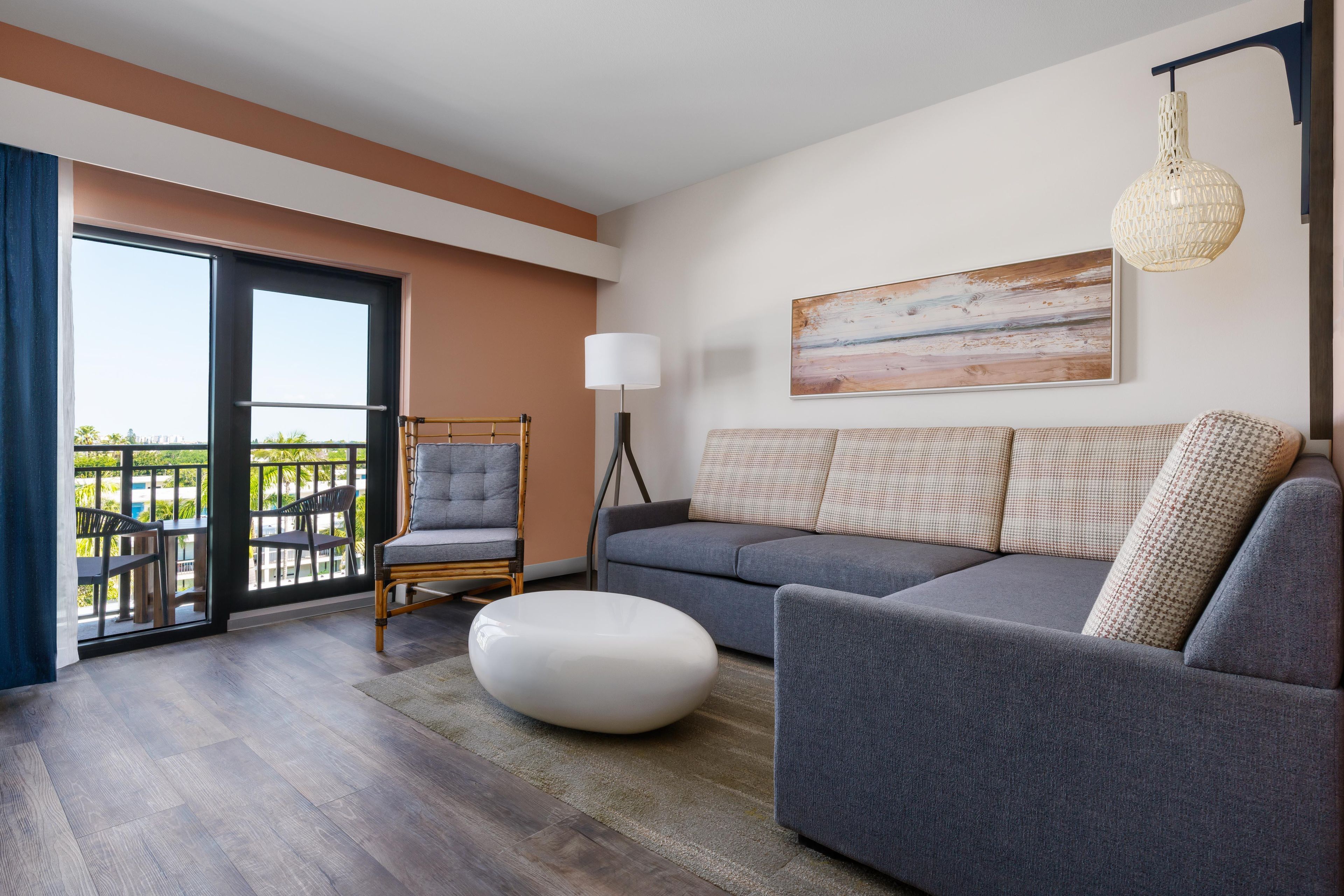 A modern living room with a grey sofa, a round ottoman, a wicker chair, and a floor lamp.