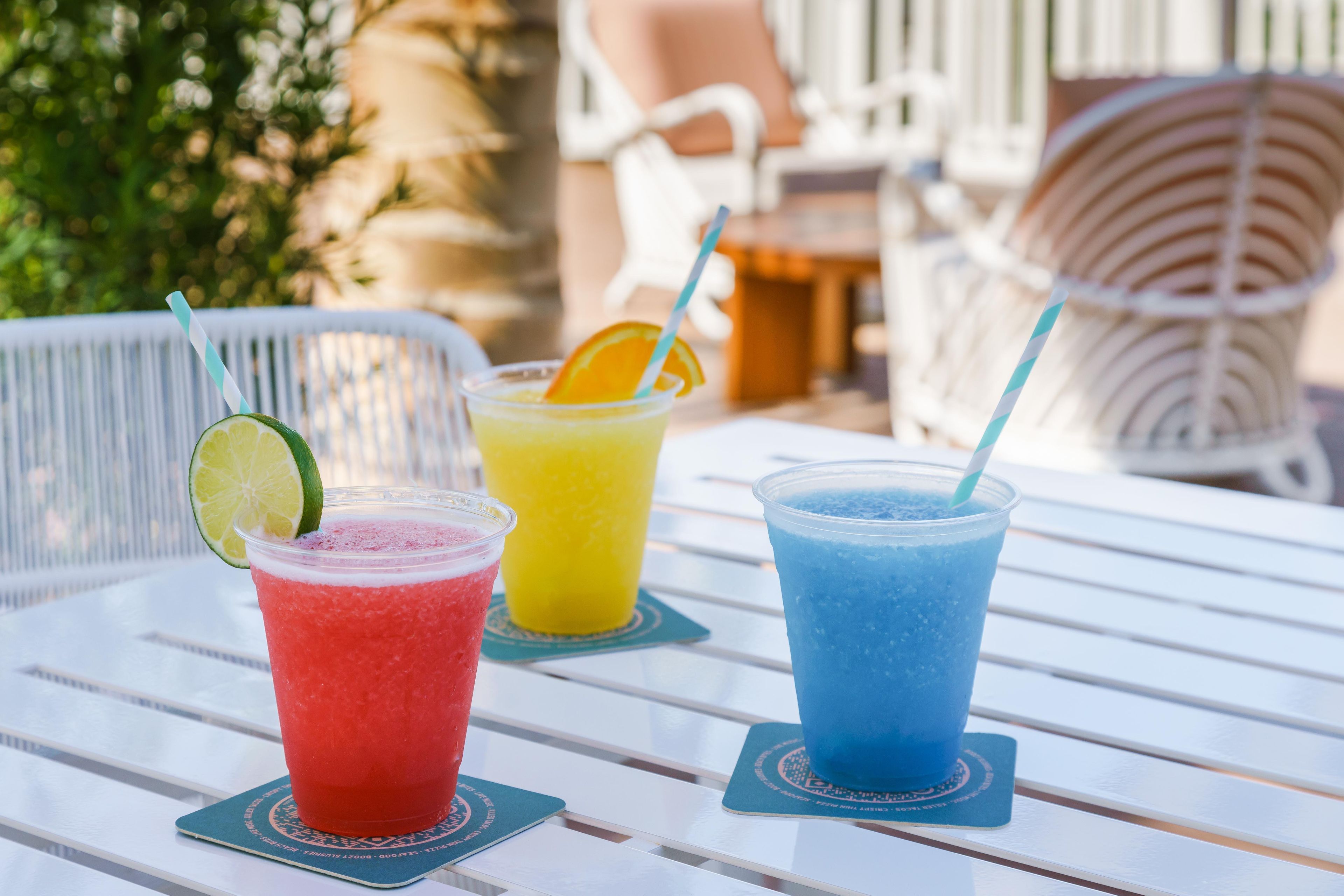 Trois boissons sur une table blanche, avec une chaise en métal en arrière-plan.