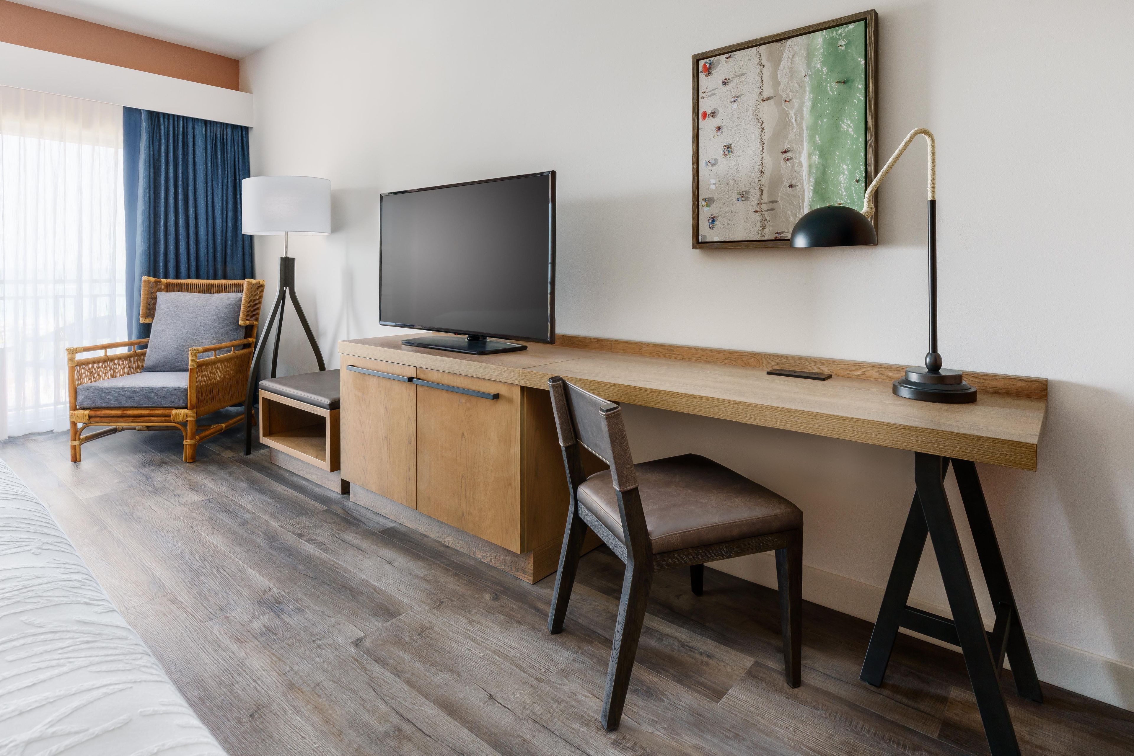 A hotel room with a wooden desk, a television, a chair, and a bed.