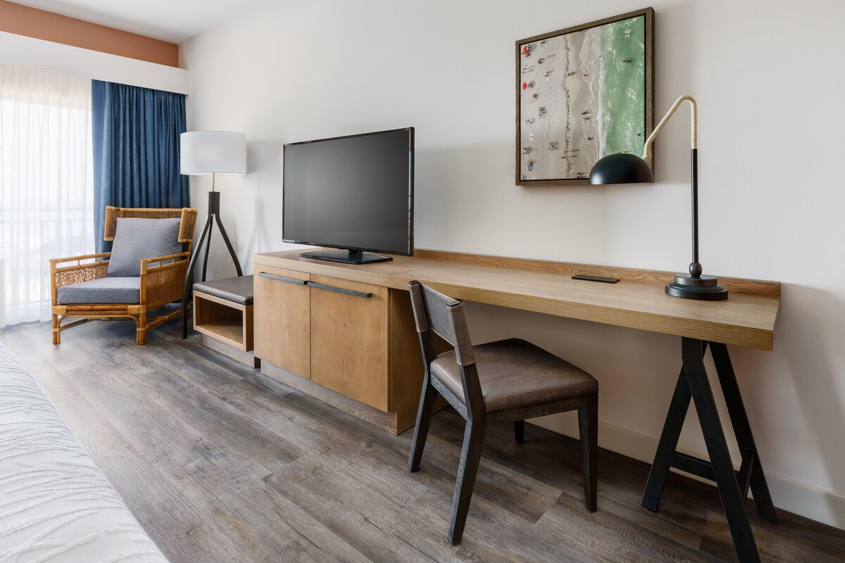 A hotel room with a wooden desk, a television, a chair, and a bed.