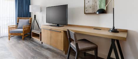 A hotel room with a wooden desk, a television, a chair, and a bed.