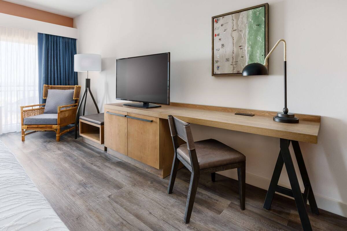 Une chambre d’hôtel avec un bureau en bois, une télévision, une chaise, une lampe et un lit.
