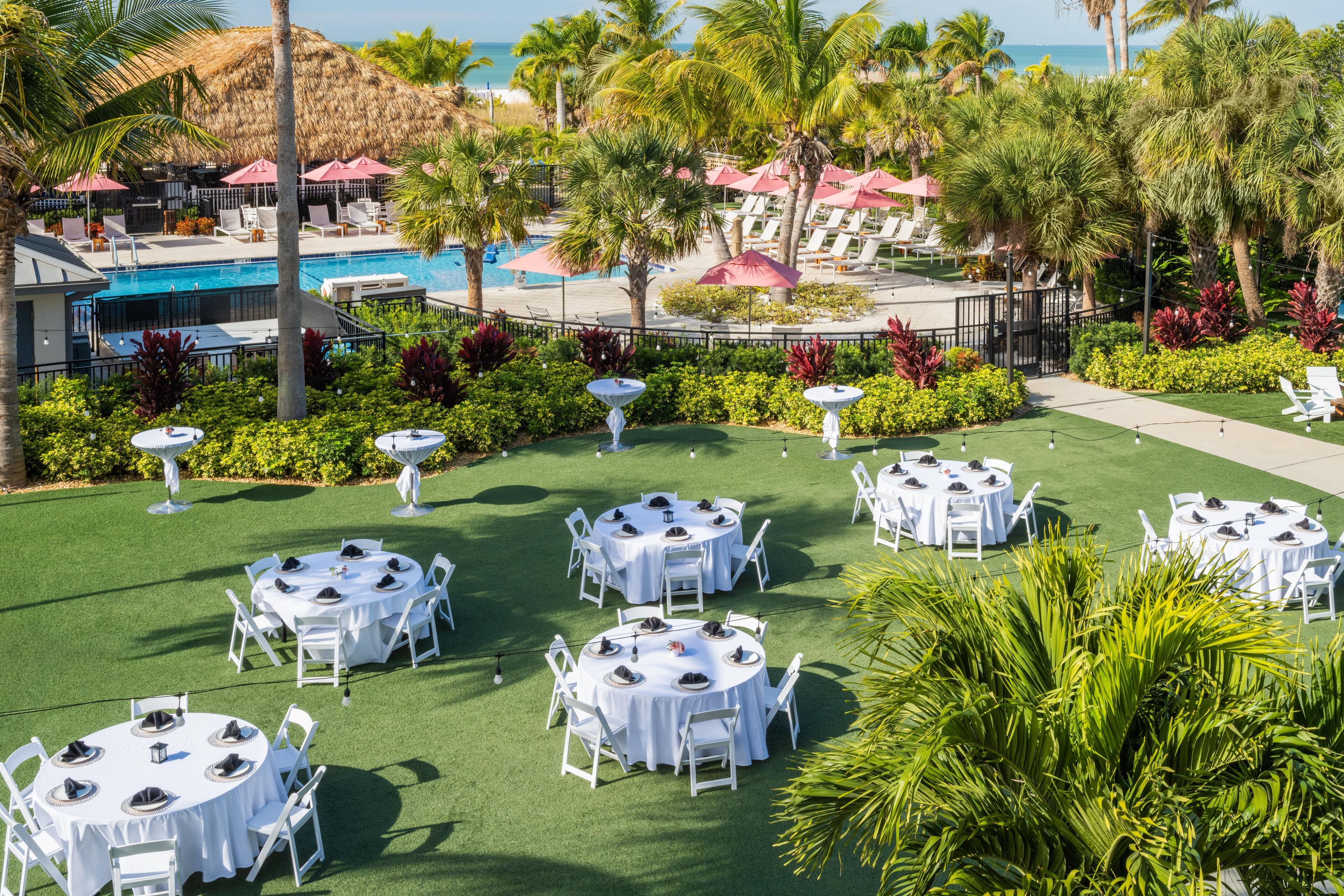Un resort con varias mesas redondas preparadas para comer, una piscina y palmeras.