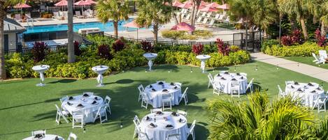 A resort with multiple round tables set for dining, a swimming pool, and palm trees.