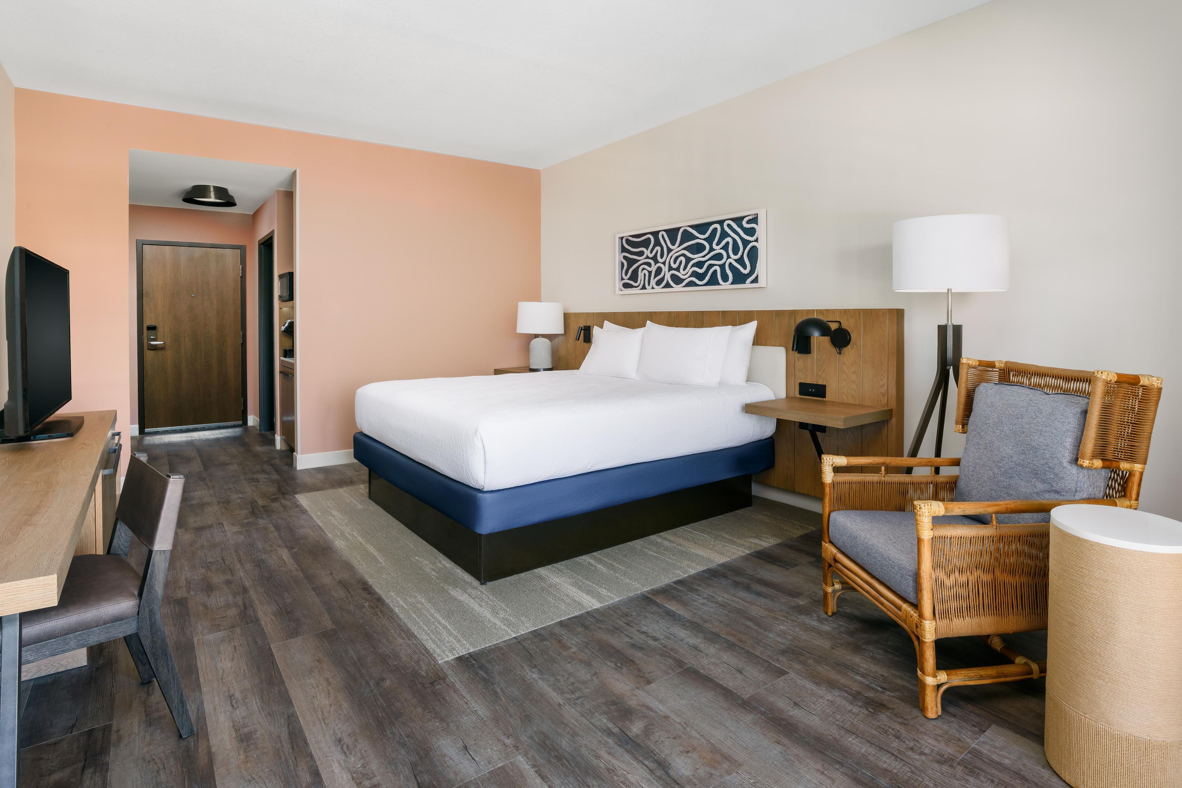 Une chambre d’hôtel avec un lit, un bureau, une chaise, une télévision et une porte.