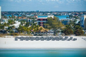 Une plage bordée de rangées de chaises longues, avec un bâtiment à toit rouge en arrière-plan.