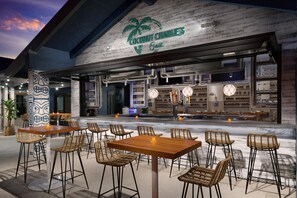 An outdoor seating area with tables and chairs, a bar with a counter, and a sign for 'Coconut Charley's Grill'.