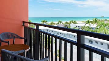 A balcony with a view of a beach, a table, and two chairs.