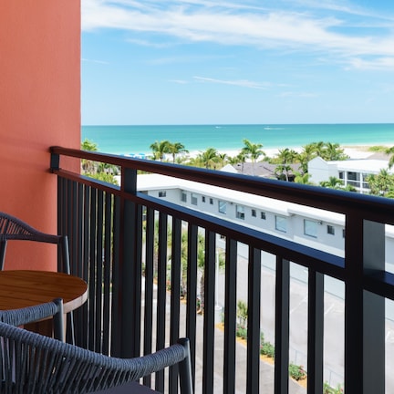 A balcony with a view of a beach, a table, and two chairs.