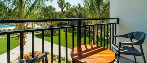 Un balcón con una mesa de madera y dos sillas, con vistas a un césped cuidado y una piscina.
