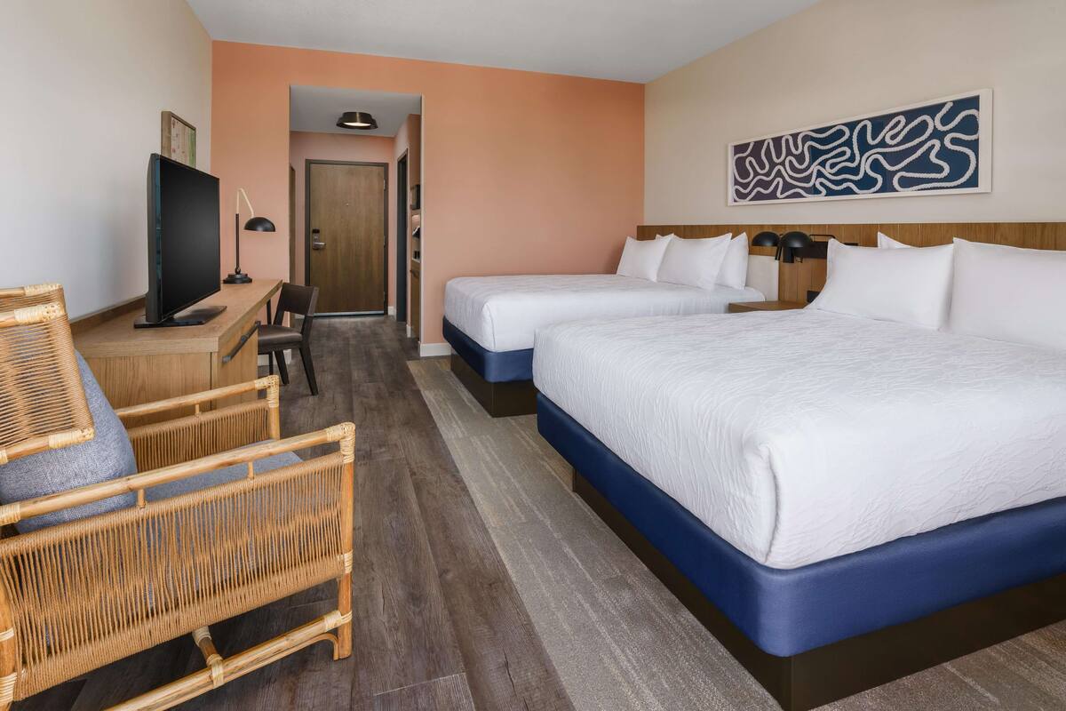 Une chambre d’hôtel avec deux lits, un bureau avec un ordinateur, une chaise et un téléviseur.
