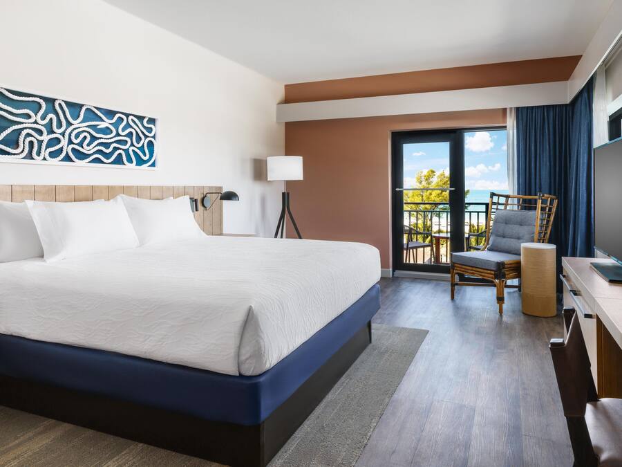 Une chambre d’hôtel avec un grand lit, un bureau avec une télévision, une chaise et un balcon avec vue.