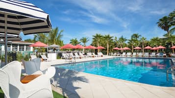 Una piscina con sillas de descanso y sombrillas, rodeada de palmeras.