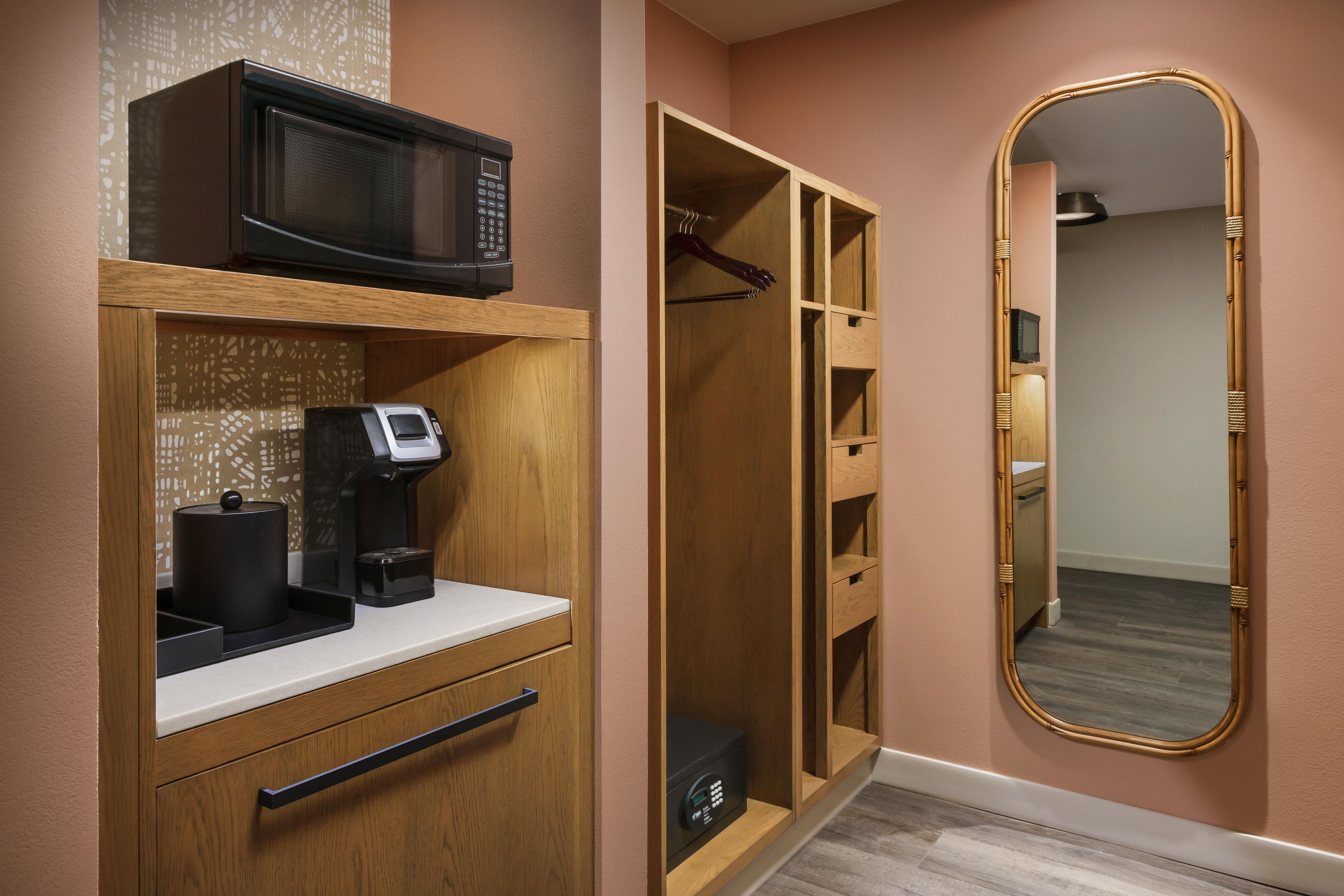 A hotel room with a minibar, a coffee machine, a mirror, and a wardrobe with multiple compartments.