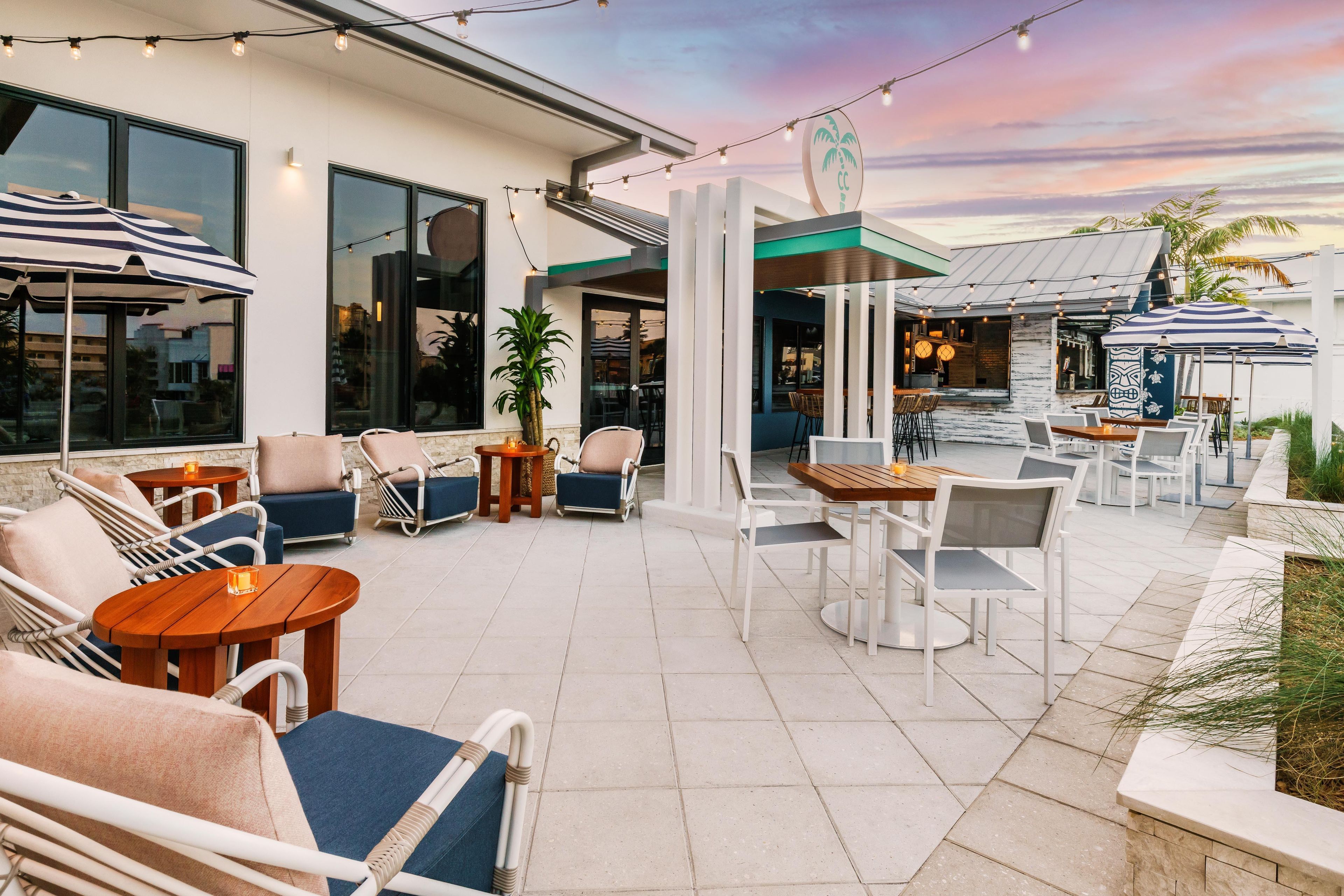 An outdoor patio area with seating arrangements, including chairs and tables, and a view of the interior through large windows.