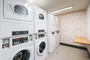 Un lavadero con lavadoras apiladas, un panel de control y una pared con pegatinas de colores.