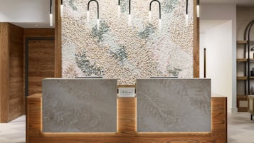 Un mostrador de recepción con acabado de madera y dos grandes mostradores rectangulares de apariencia marmórea. Sobre el mostrador, una pared con textura que recuerda a guijarros y conchas.