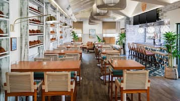 Un restaurante espacioso con mesas y sillas de madera, una zona de bar y estantes con objetos decorativos.
