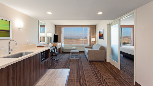 A hotel room with a kitchenette, a sofa, a bed, and a large window offering a view of the landscape. - Holiday Inn Diamond Bar - Pomona by IHG (Diamond Bar)