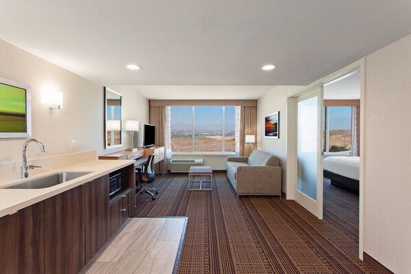 A hotel room with a kitchenette, a sofa, a bed, and a large window offering a view of the landscape. - Holiday Inn Diamond Bar - Pomona by IHG (Diamond Bar)