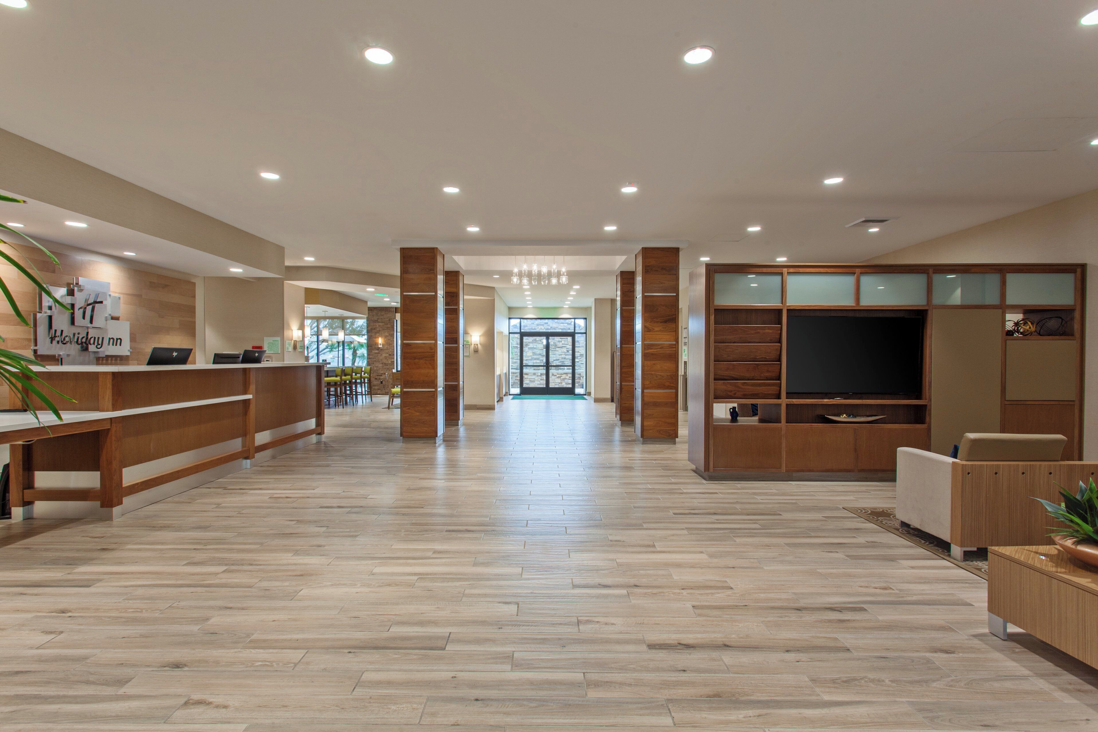 A spacious lobby with wooden reception desks, a seating area, and a large television screen.