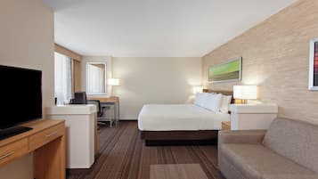 Habitación de hotel con cama, escritorio, televisor, sofá y un cuadro en la pared.