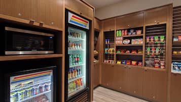A kitchen with a microwave, refrigerator, and pantry stocked with snacks and condiments.