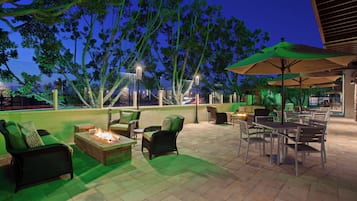 An outdoor patio area with seating, a fire pit, and a view of the cityscape at dusk.
