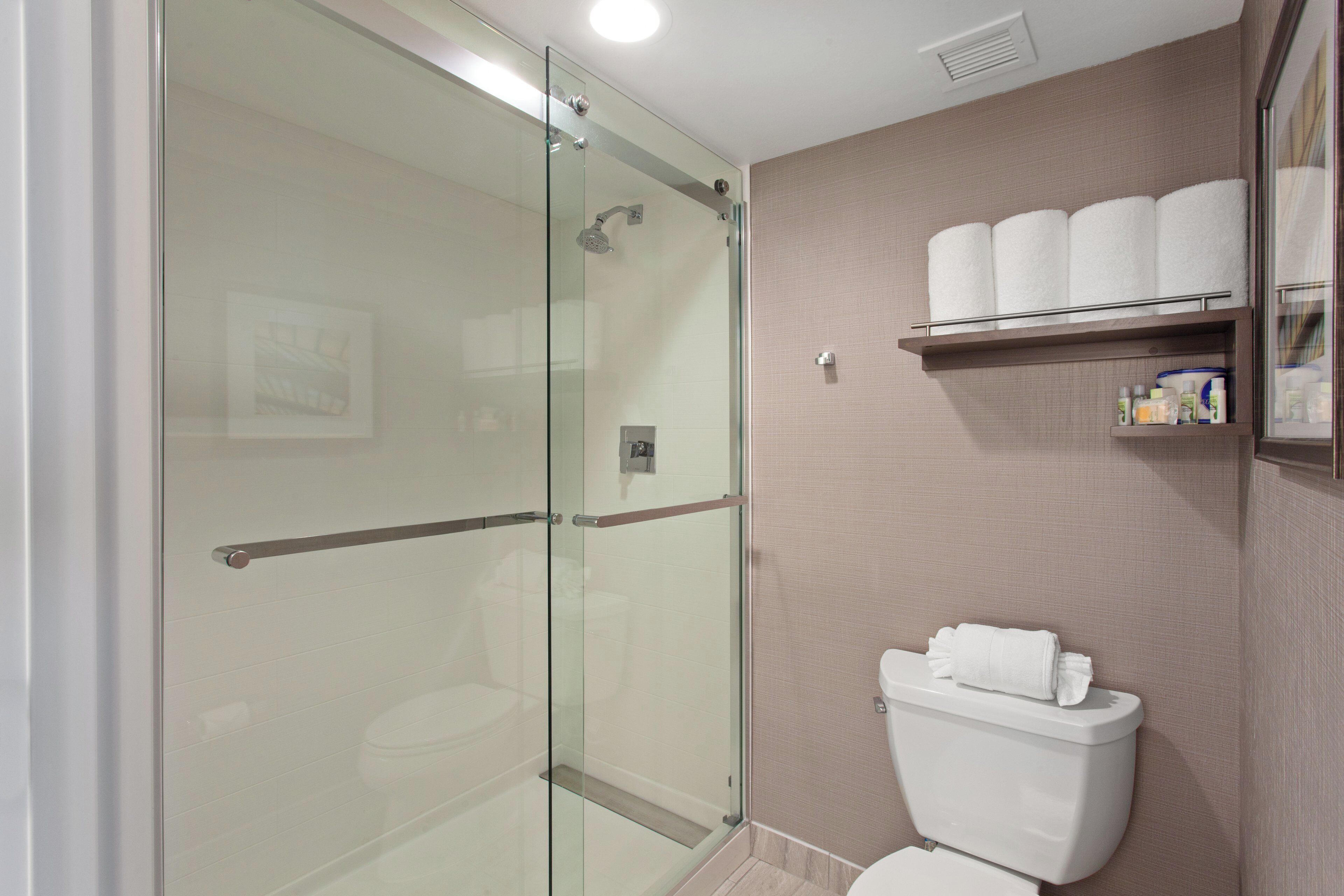 A bathroom with a glass shower enclosure, a toilet, and a shelf with toiletries.