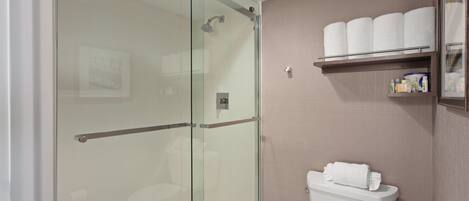 A bathroom with a glass shower enclosure, a toilet, and a shelf with toiletries.