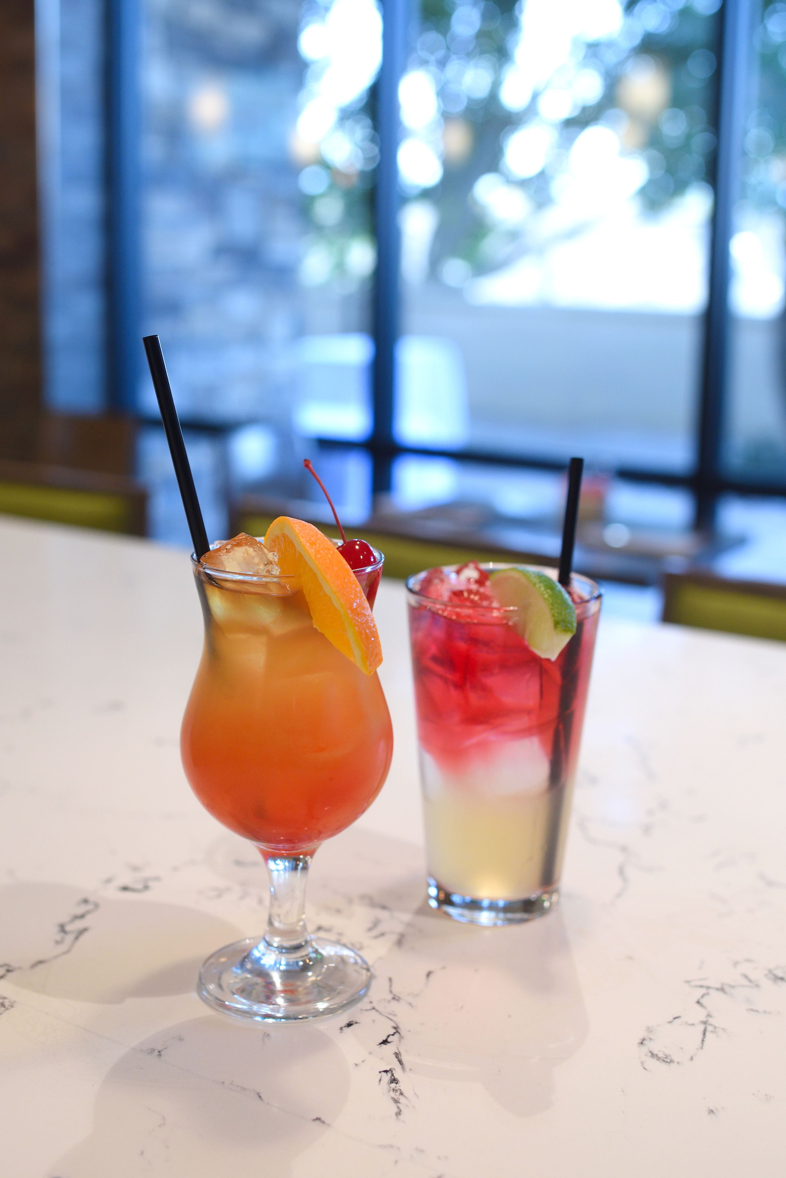 Two cocktails on a marble table with a blurred background of a window and interior.
